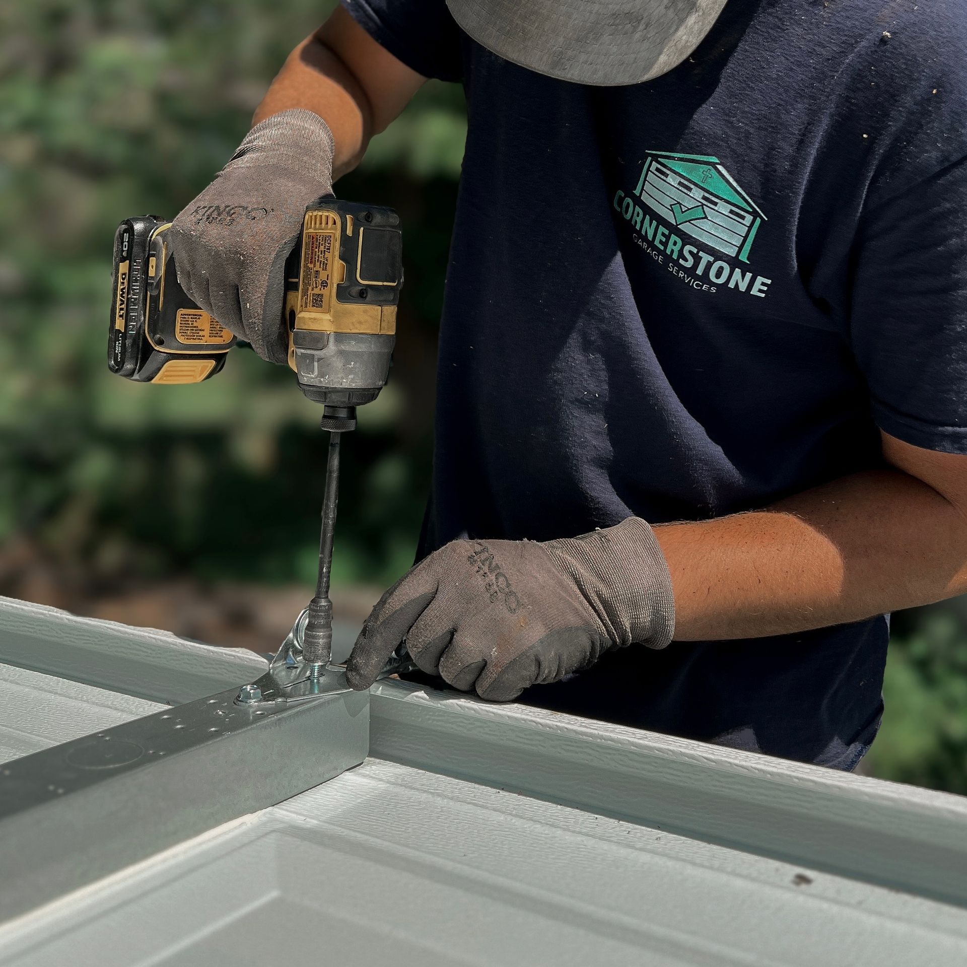 Person in gloves using a drill on a structure, likely construction, outdoors.