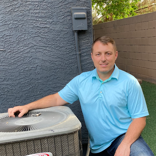 A man in a blue shirt is sitting next to an air conditioner.