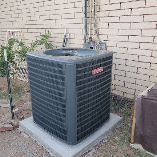 An air conditioner is sitting on a concrete base in front of a brick wall.
