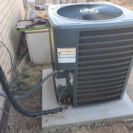 A gray air conditioner is sitting on a concrete block next to a brick wall