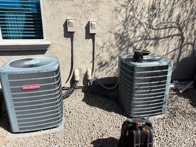 Two air conditioners are sitting next to each other on the side of a house.