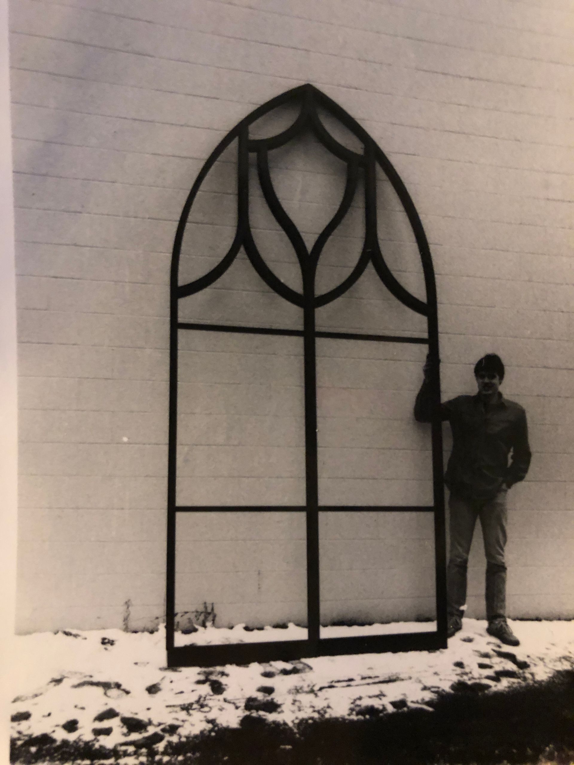 A black and white photo of a man standing in front of a large window