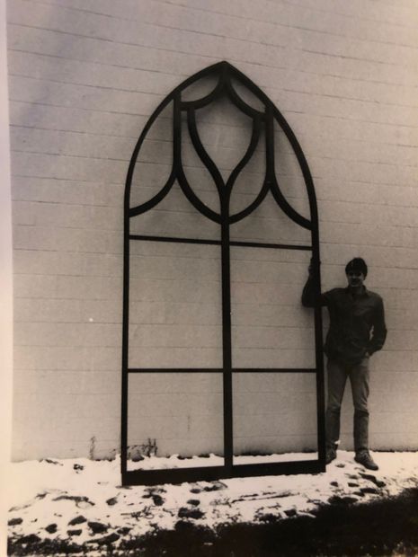 A black and white photo of a man standing in front of a large window
