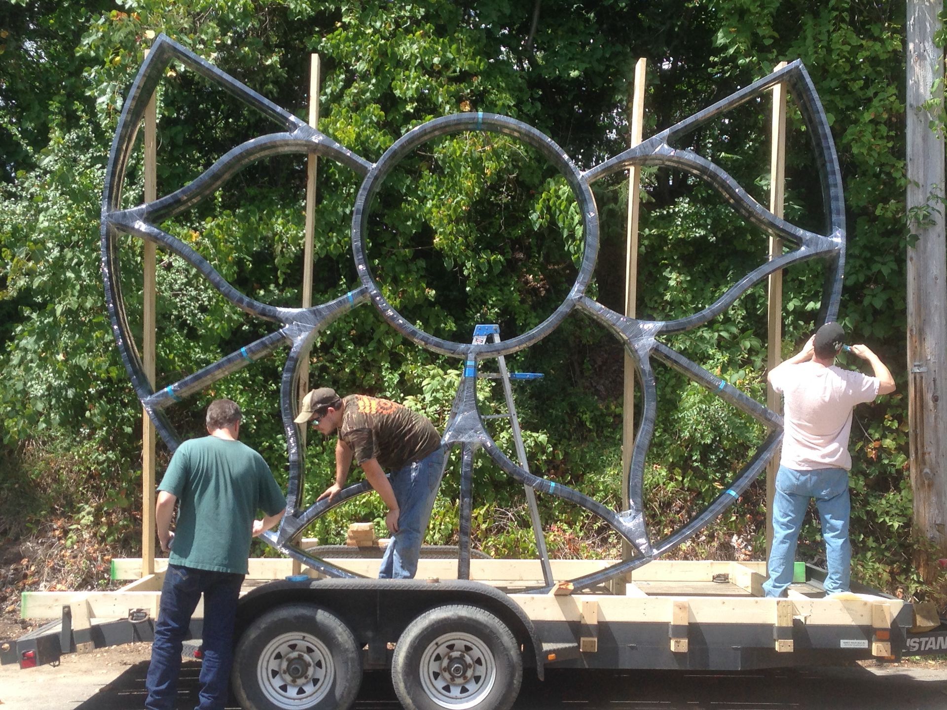Three men are working on a large metal structure on a trailer.