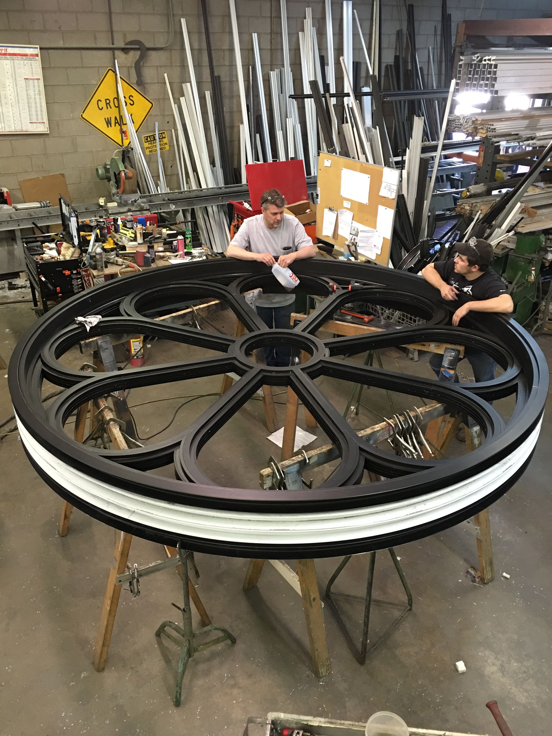 Two men are working on a large wheel in a factory.