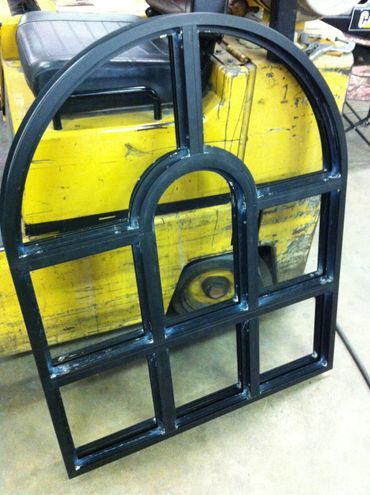 A black metal window frame is sitting on a concrete floor.