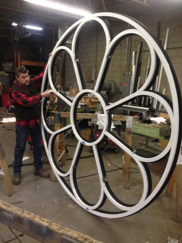 A man is standing next to a large circular object in a workshop.
