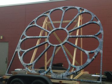 A large metal wheel is on a trailer in front of a building