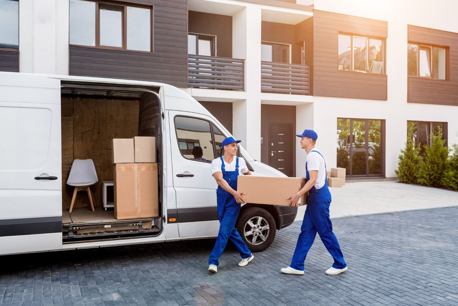 Two movers are loading boxes into a van in front of a building.