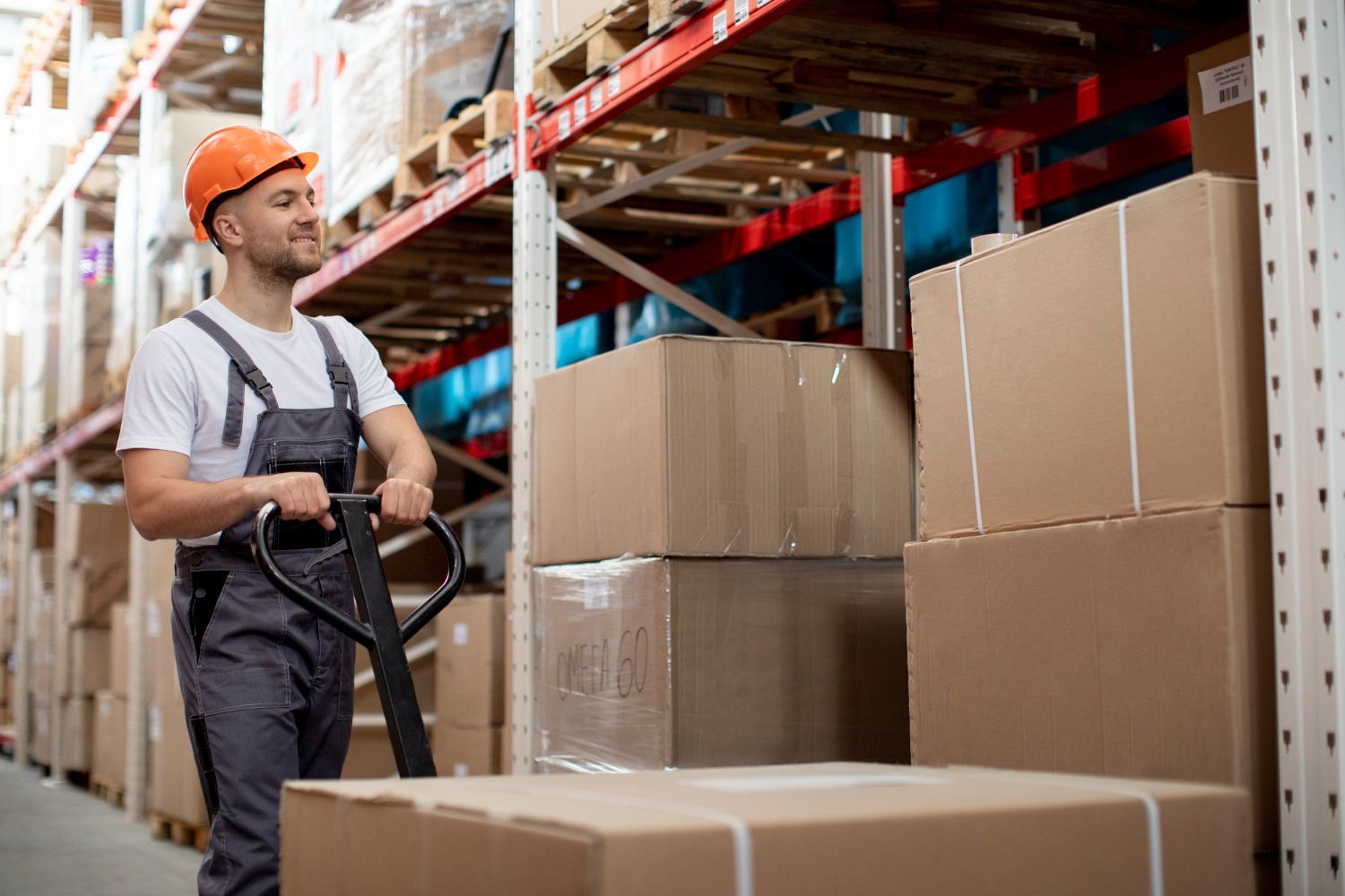 A man is pushing a pallet truck in a warehouse filled with boxes.