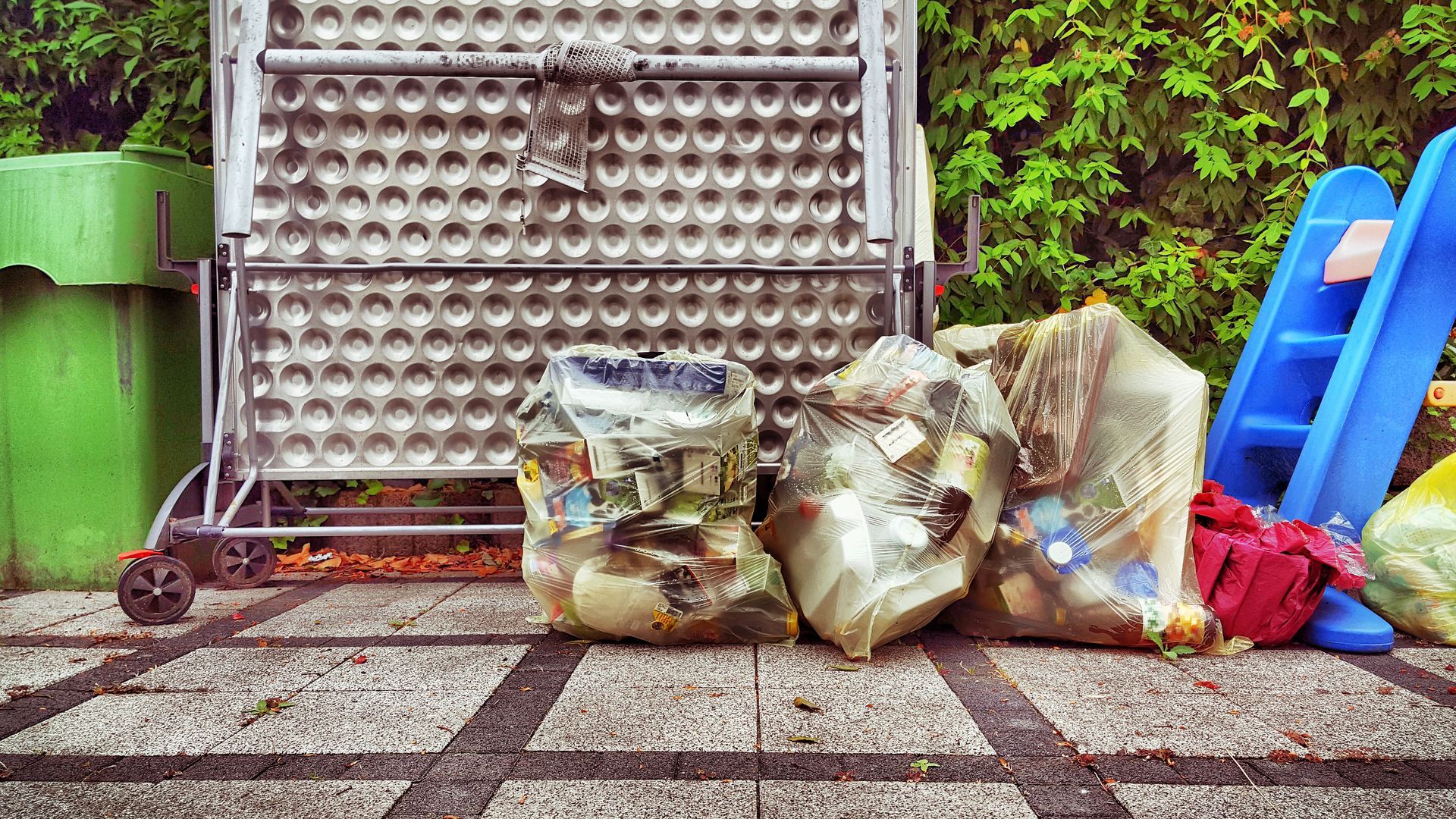 A pile of trash is sitting on a sidewalk next to a green trash can.