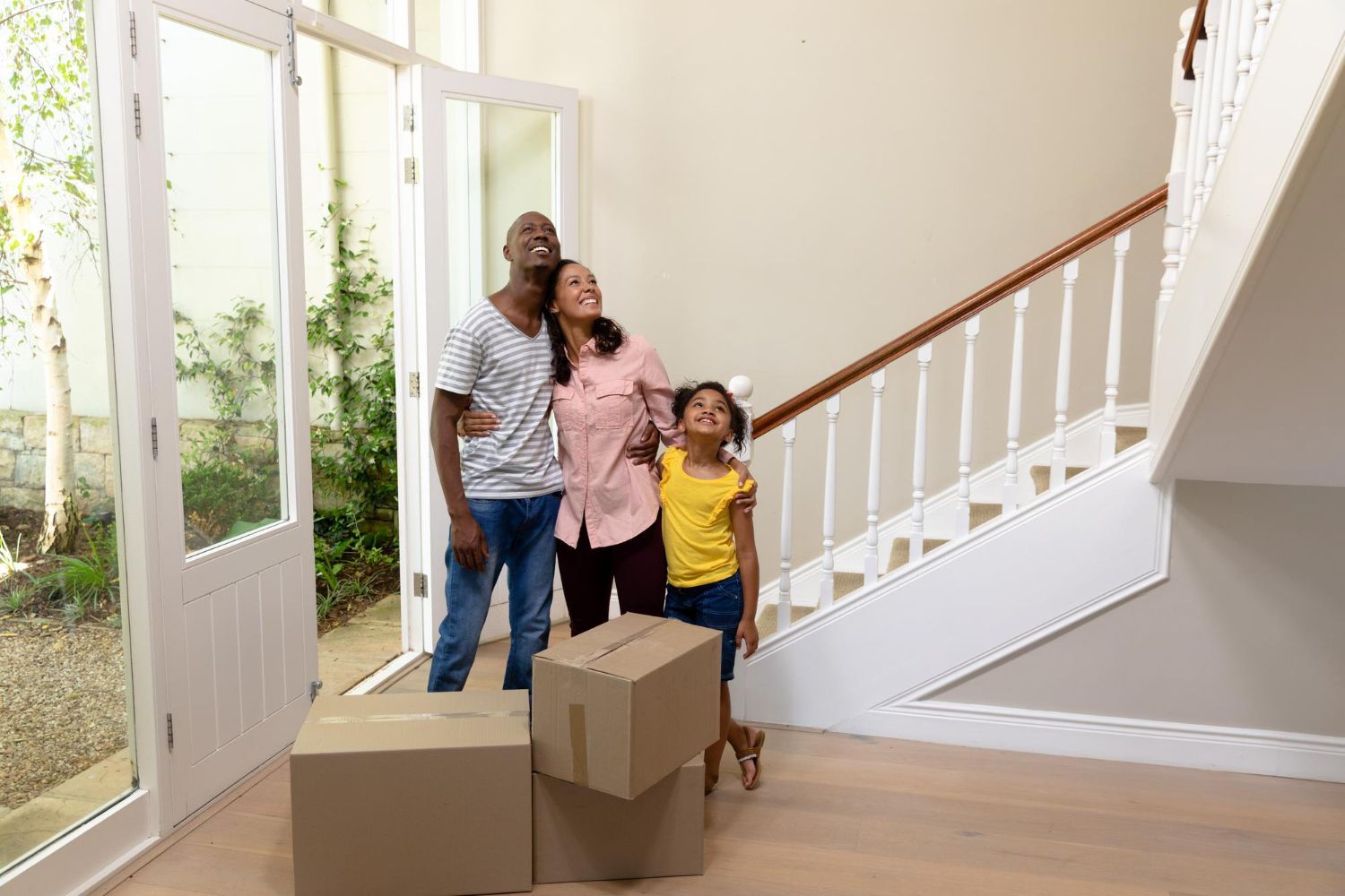 A family is standing in front of a staircase in their new home.