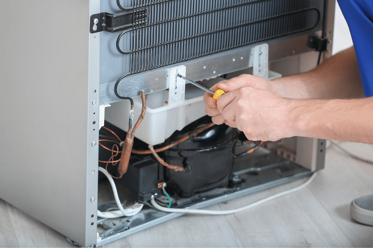 Person repairing the back of a refrigerator with a screwdriver.