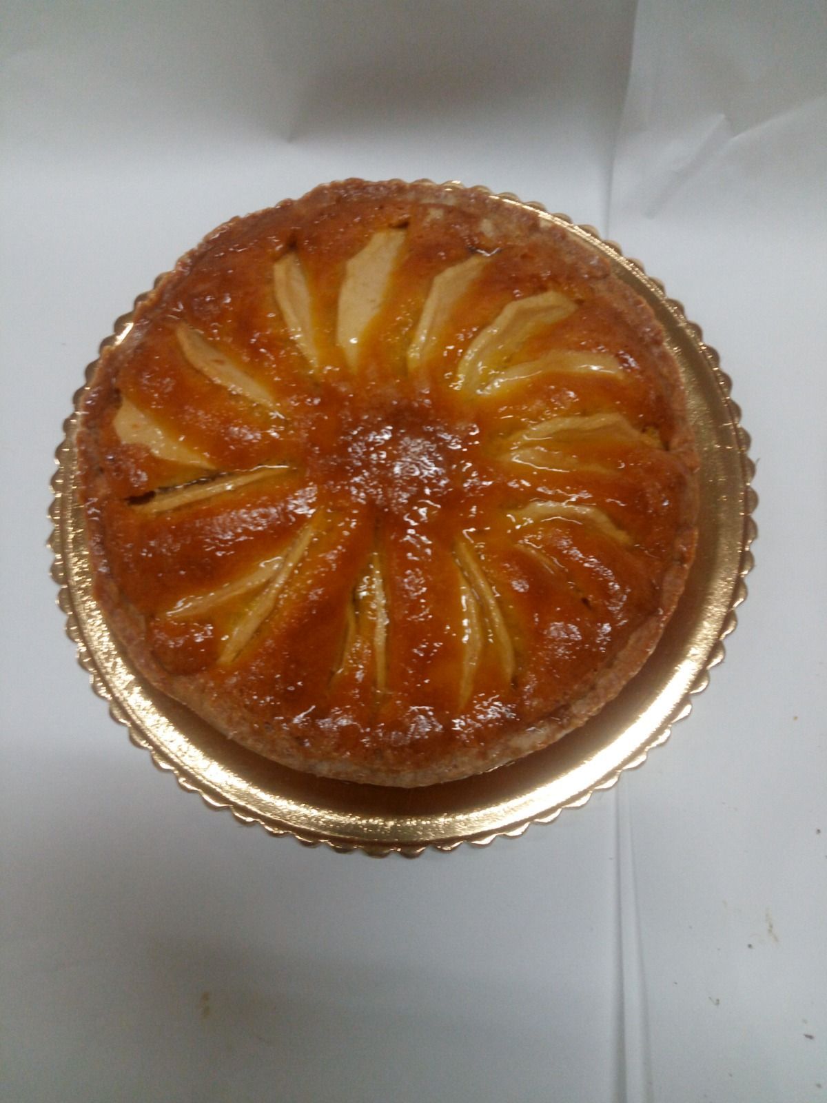 Crostata di frutta rotonda con glassa al caramello, cotta in una tortiera di alluminio dorato su una superficie bianca.