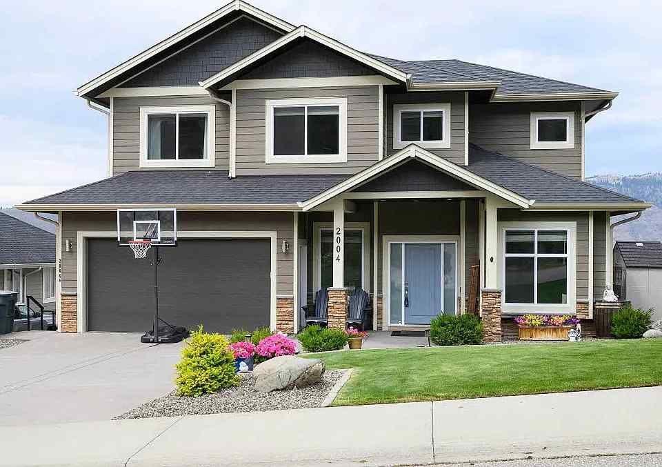 Two-story suburban house with gray horizontal siding, dark gray roof, a basketball hoop on the driveway, and a front lawn.