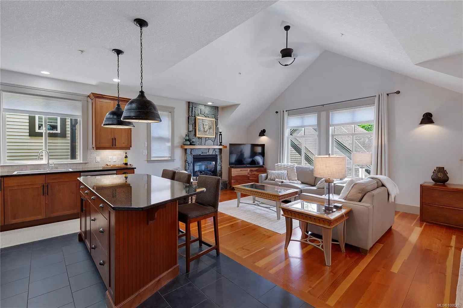 A modern open-plan home interior featuring a kitchen island, dining area, and living room with a fireplace and wood floors.