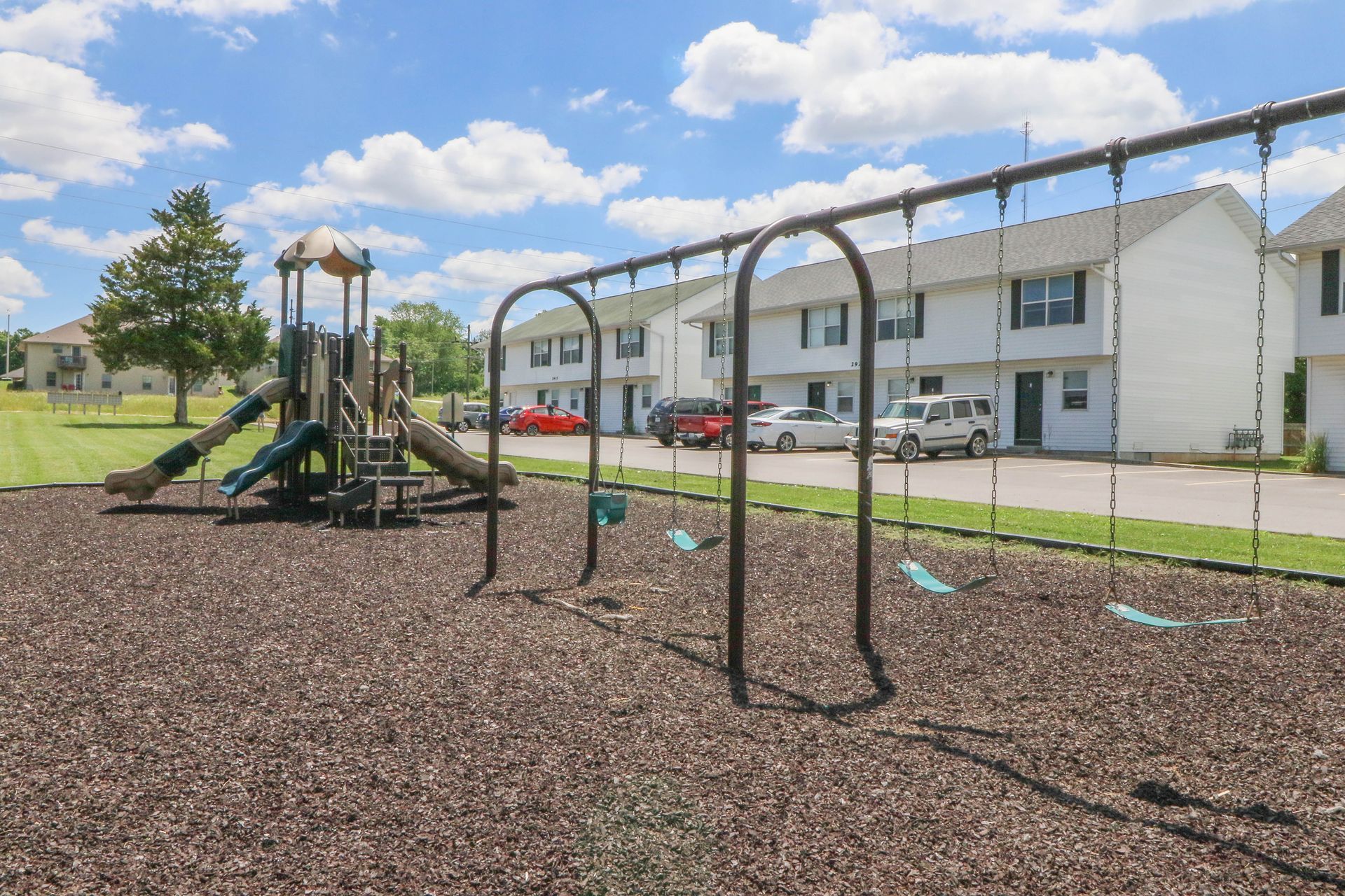A playground with swings and a slide in front of a building.