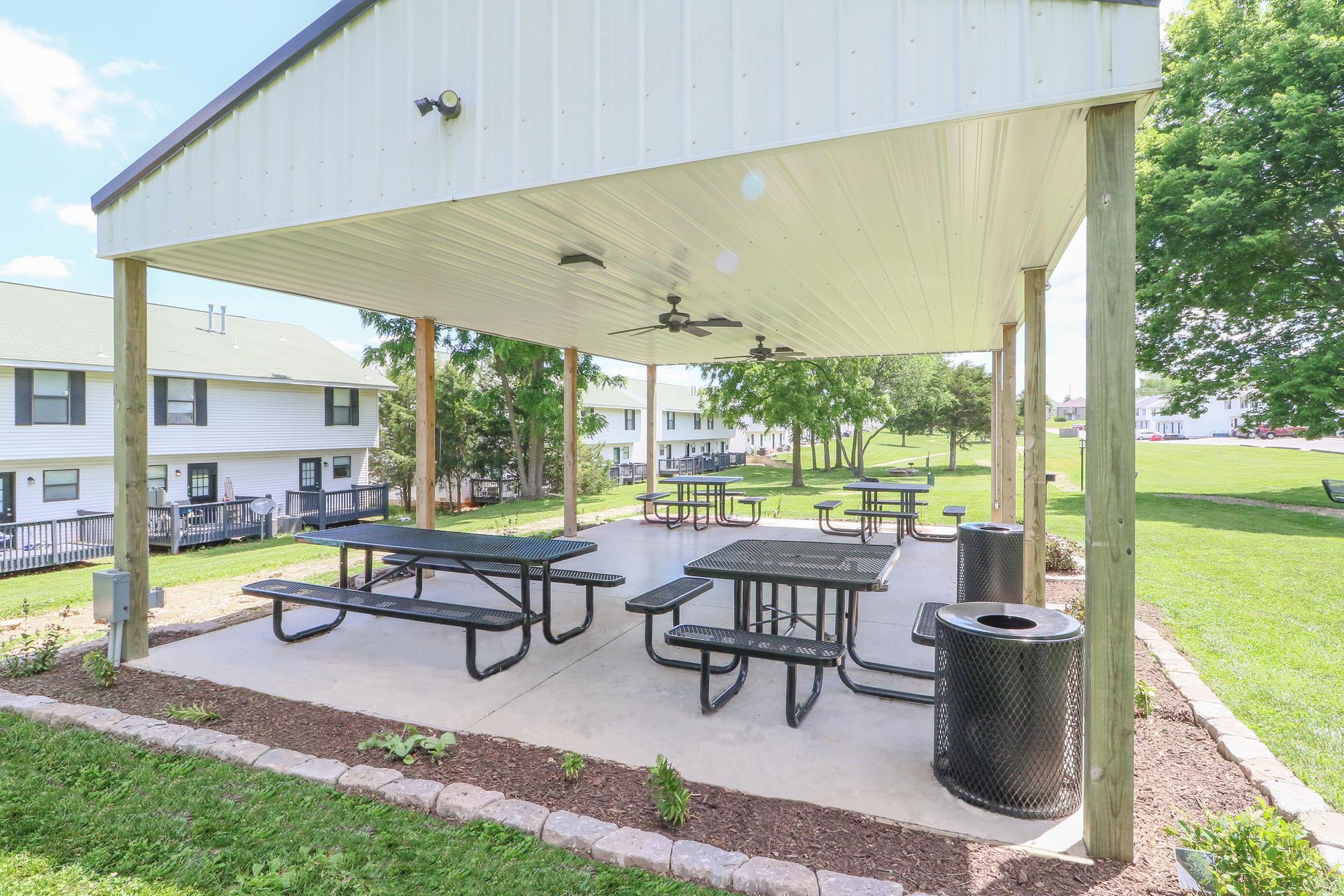 A picnic area with tables and a trash can under a covered shelter.