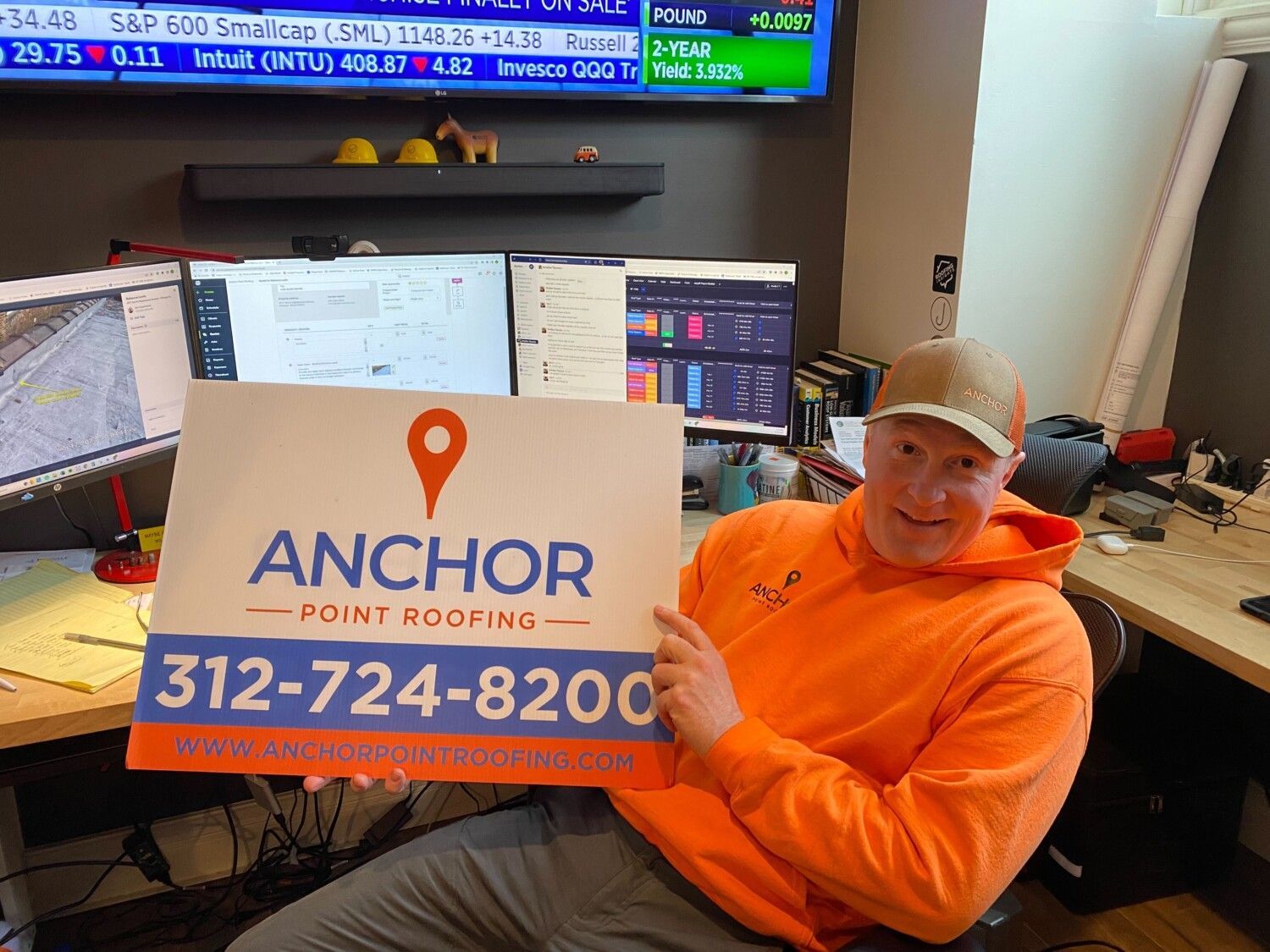 A man is sitting at a desk holding a sign that says anchor point roofing.