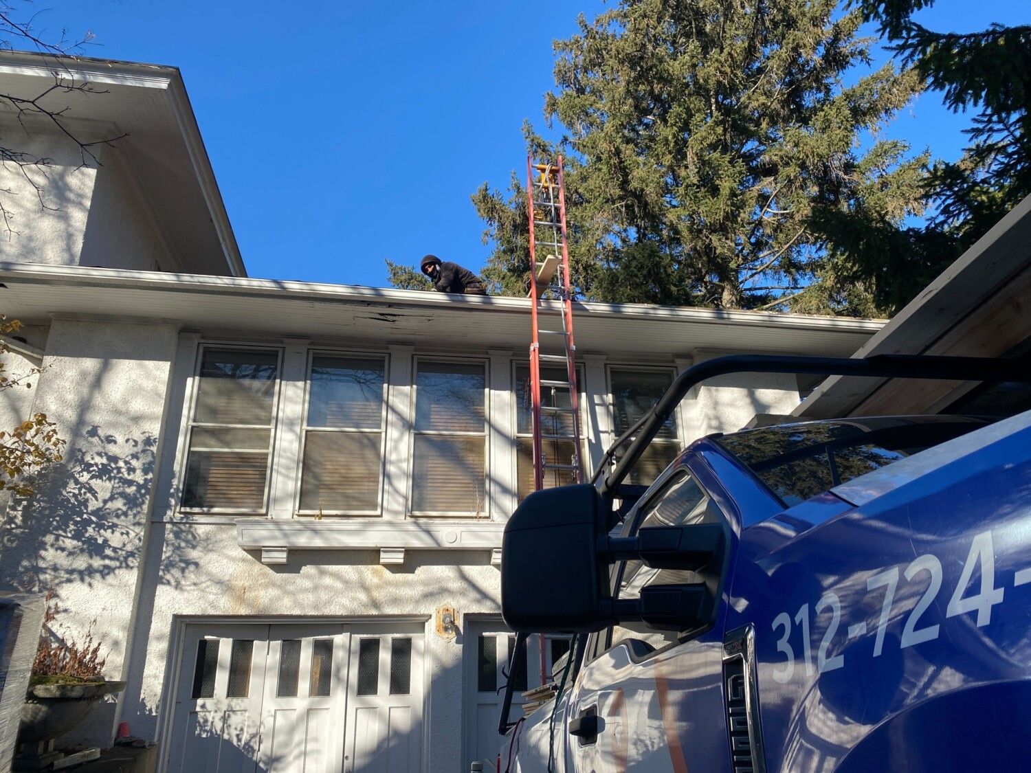 A man on a ladder is working on the roof of a house.
