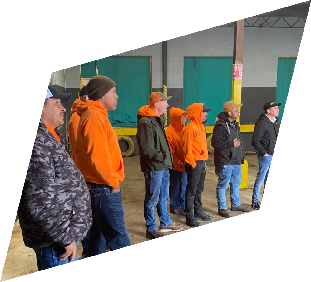 A group of men in orange hoodies are standing in a warehouse.