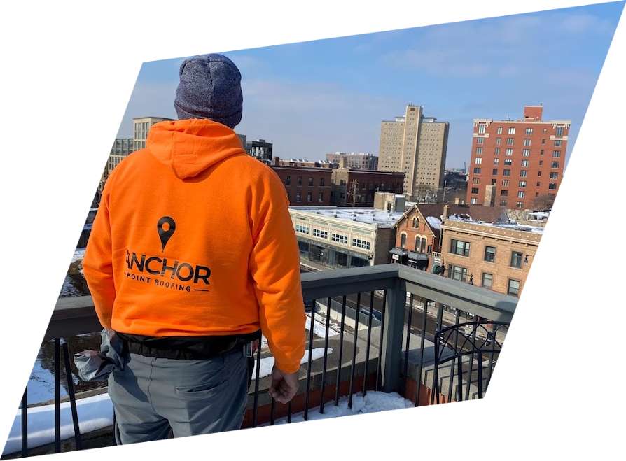 A man wearing an orange anchor sweatshirt stands on a balcony overlooking a city.