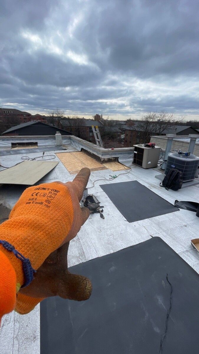 A person wearing orange gloves is pointing at a roof.
