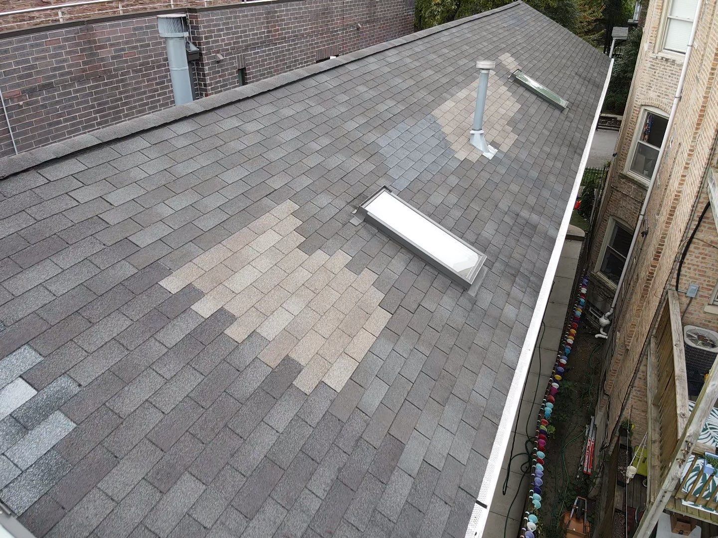 An aerial view of a roof with shingles missing and a skylight.