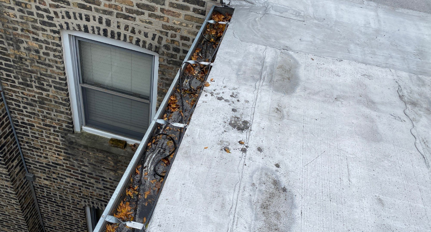 A gutter with leaves on it is on the roof of a building next to a window.