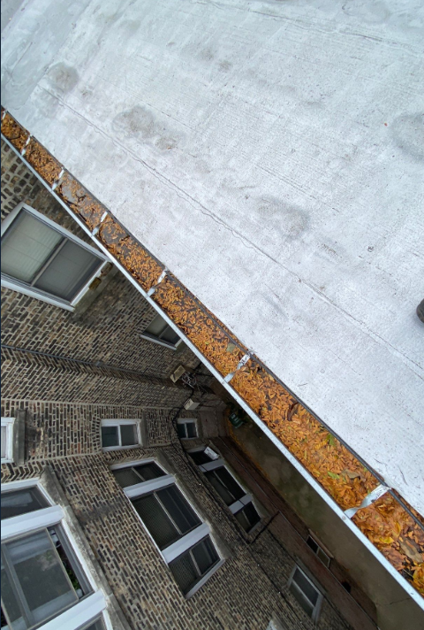 A roof with a gutter on it and a brick building in the background.