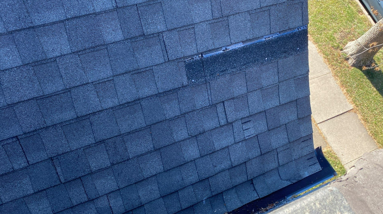 An aerial view of a roof with blue shingles and a sidewalk.