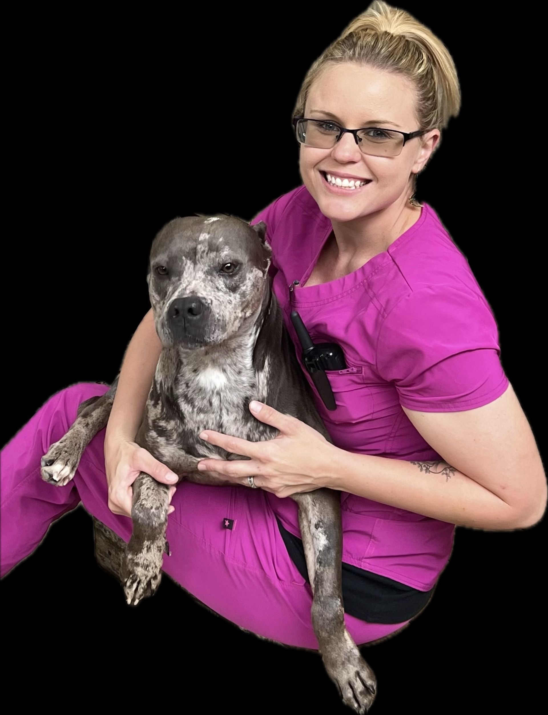 Woman in pink scrubs smiles, holding spotted dog.