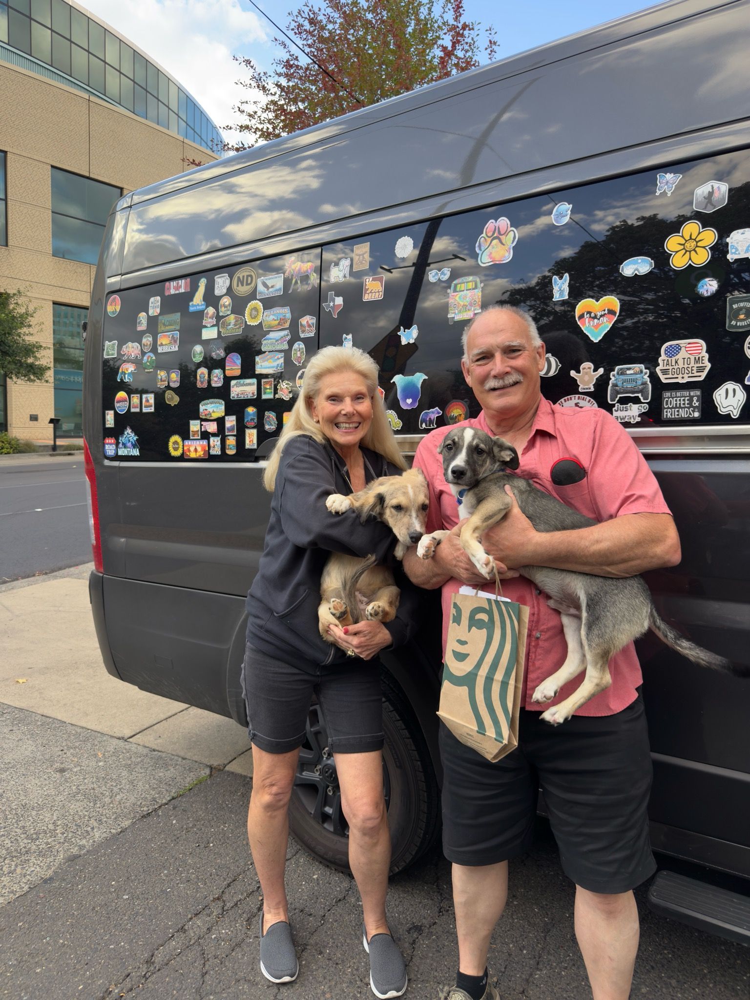 Two people holding dogs, standing next to a van with stickers.