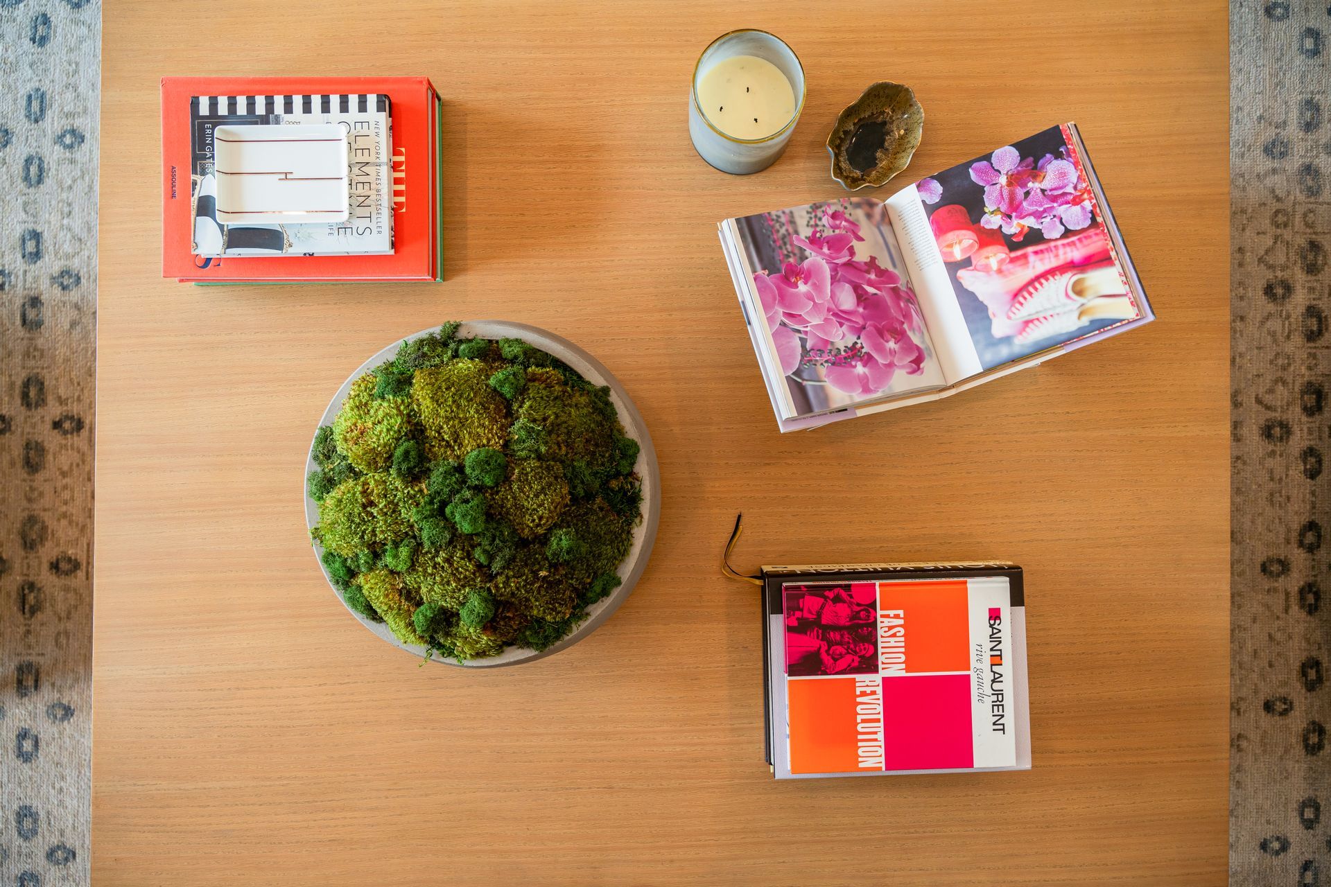 A wooden coffee table with a bowl of moss , a book , and a candle.
