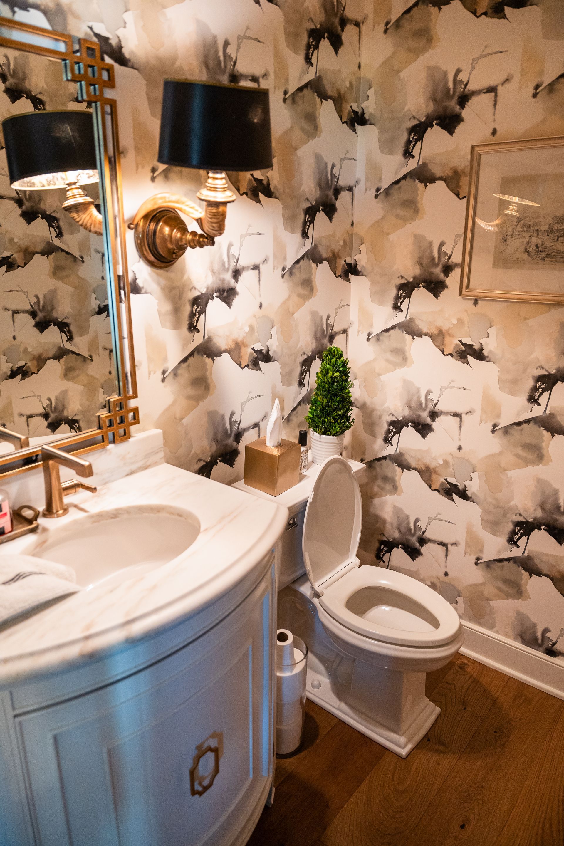 A bathroom with a toilet , sink , mirror and floral wallpaper.