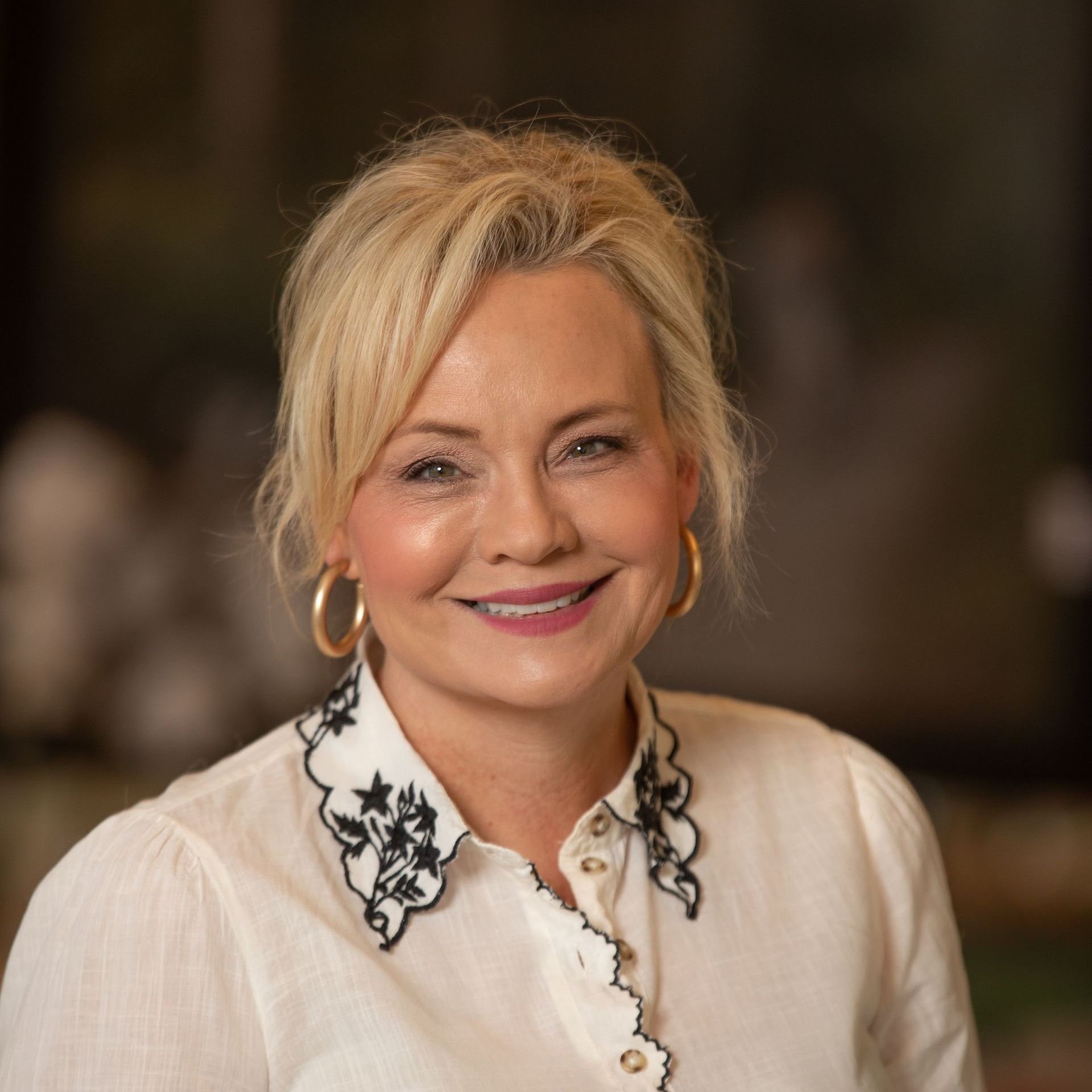 A woman wearing a white shirt with a black collar is smiling for the camera.