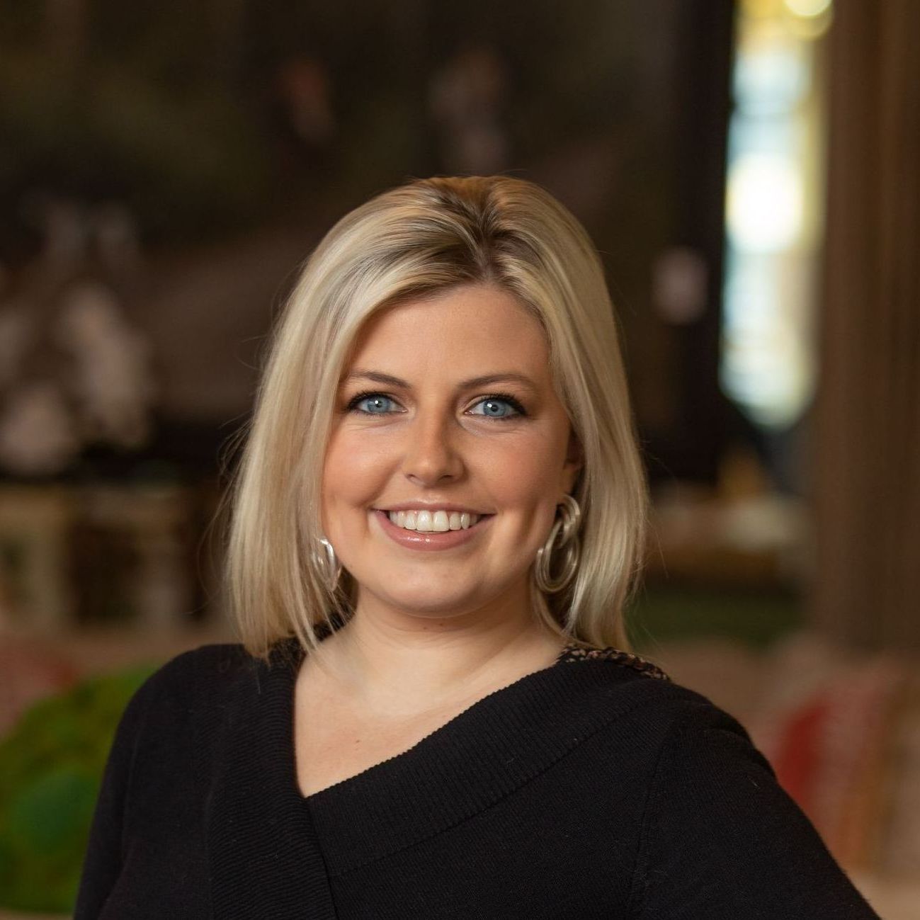 A woman wearing a black sweater and hoop earrings is smiling for the camera.