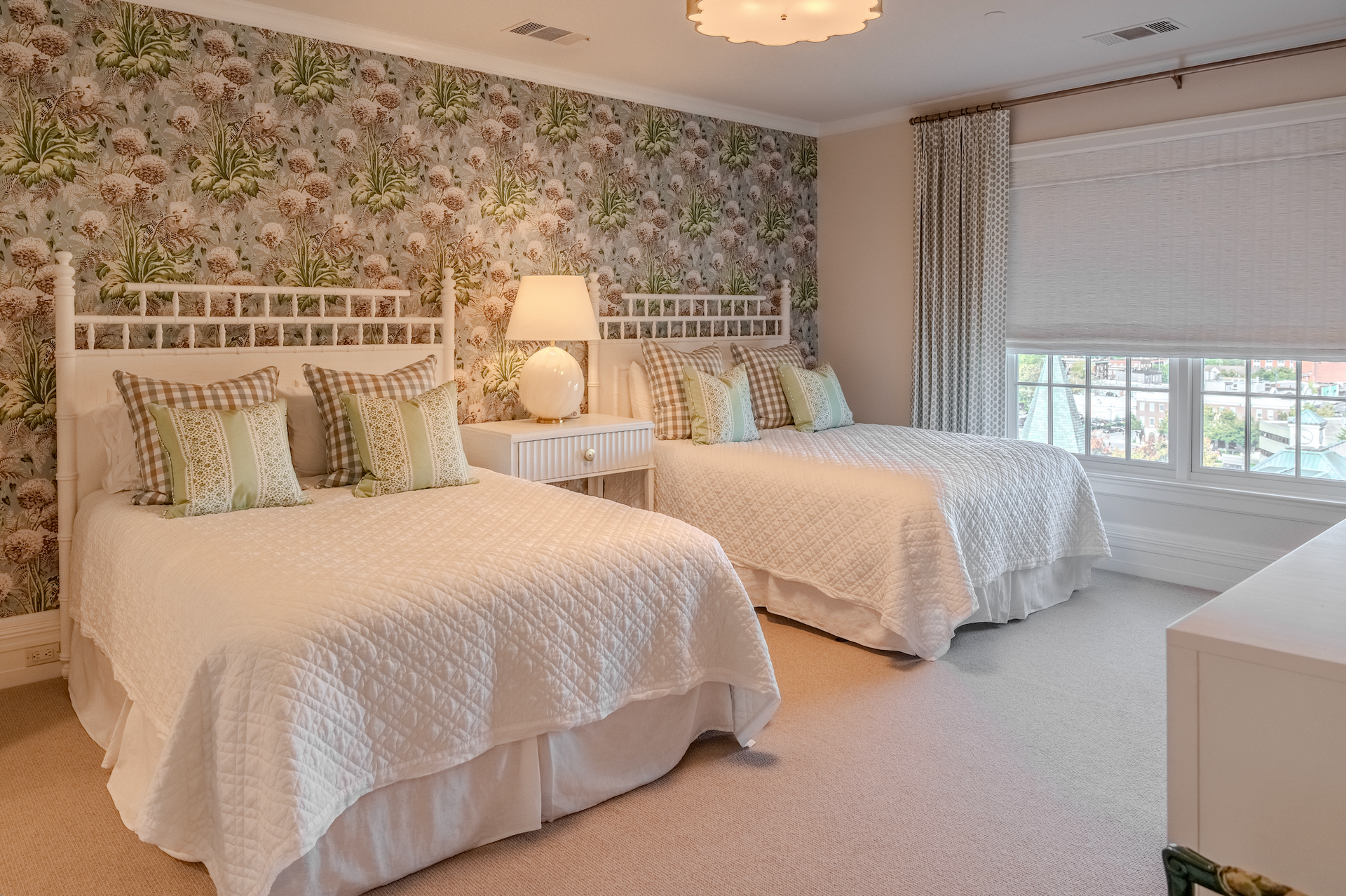 A bedroom with two beds and a floral wallpaper on the wall.