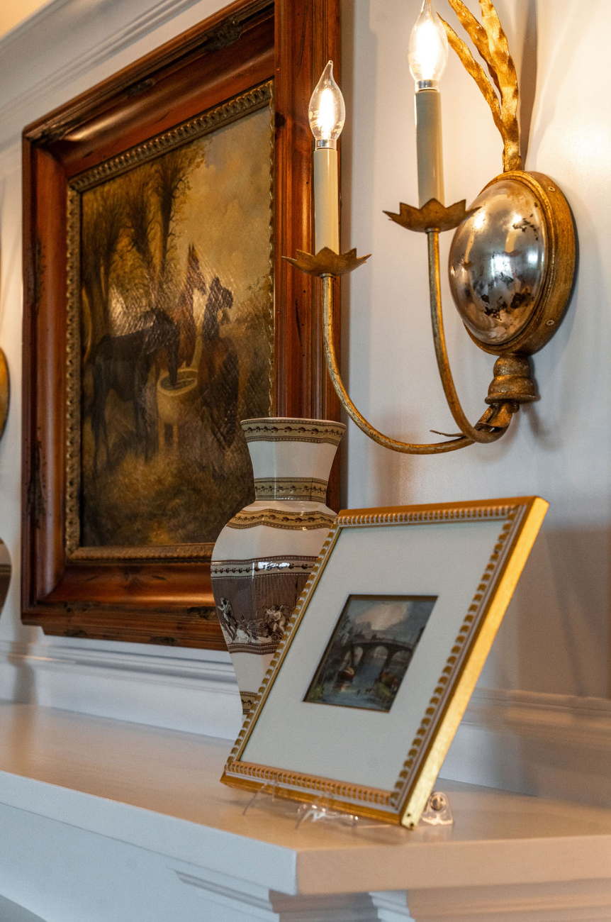A framed picture is sitting on a mantle next to a painting.
