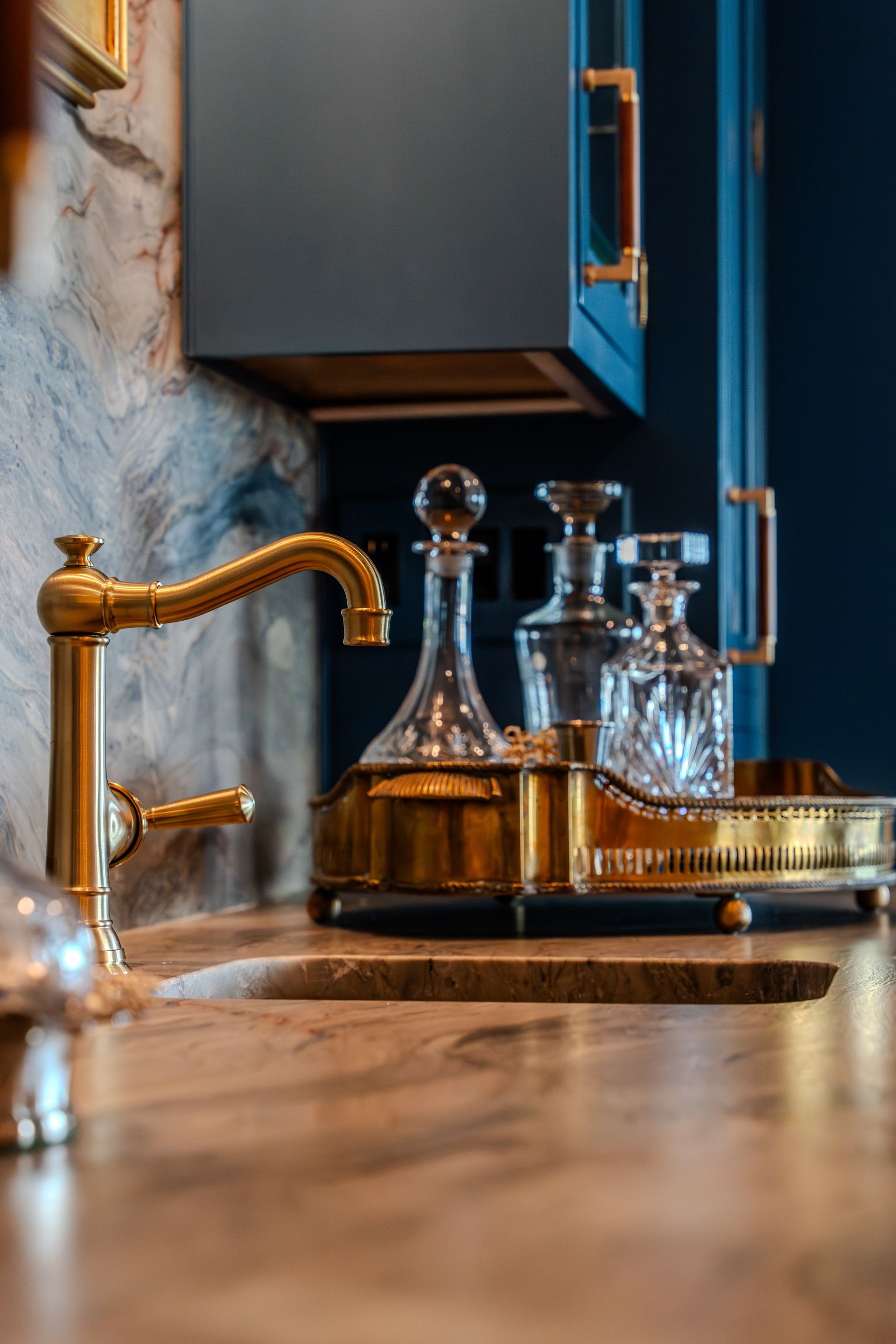 A kitchen sink with a gold faucet and a tray with bottles and glasses on it.