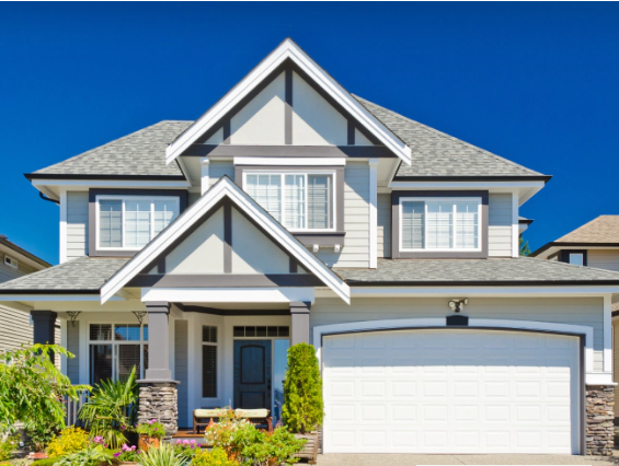 Two-story house with gray siding, white trim, and a white garage door against a bright blue sky.