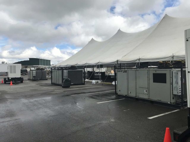 Utility truck with boom extended, workers near air conditioning unit. Street scene with utility poles.