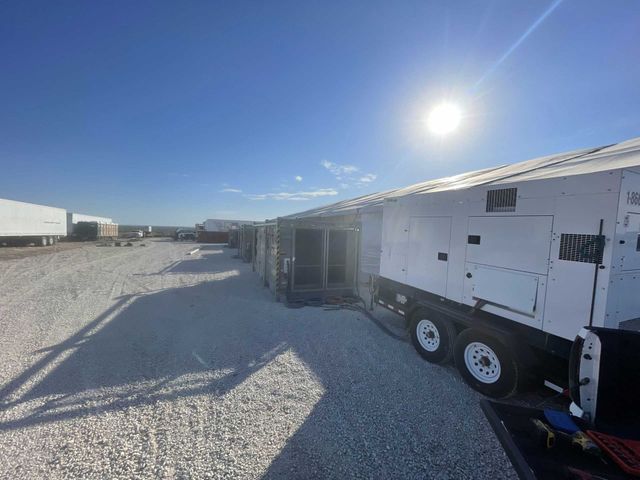 Bright sunny day, rows of white generator trailers on a gravel lot under a blue sky.