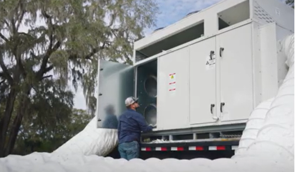 Man servicing a large white industrial unit on a trailer, with a natural background.