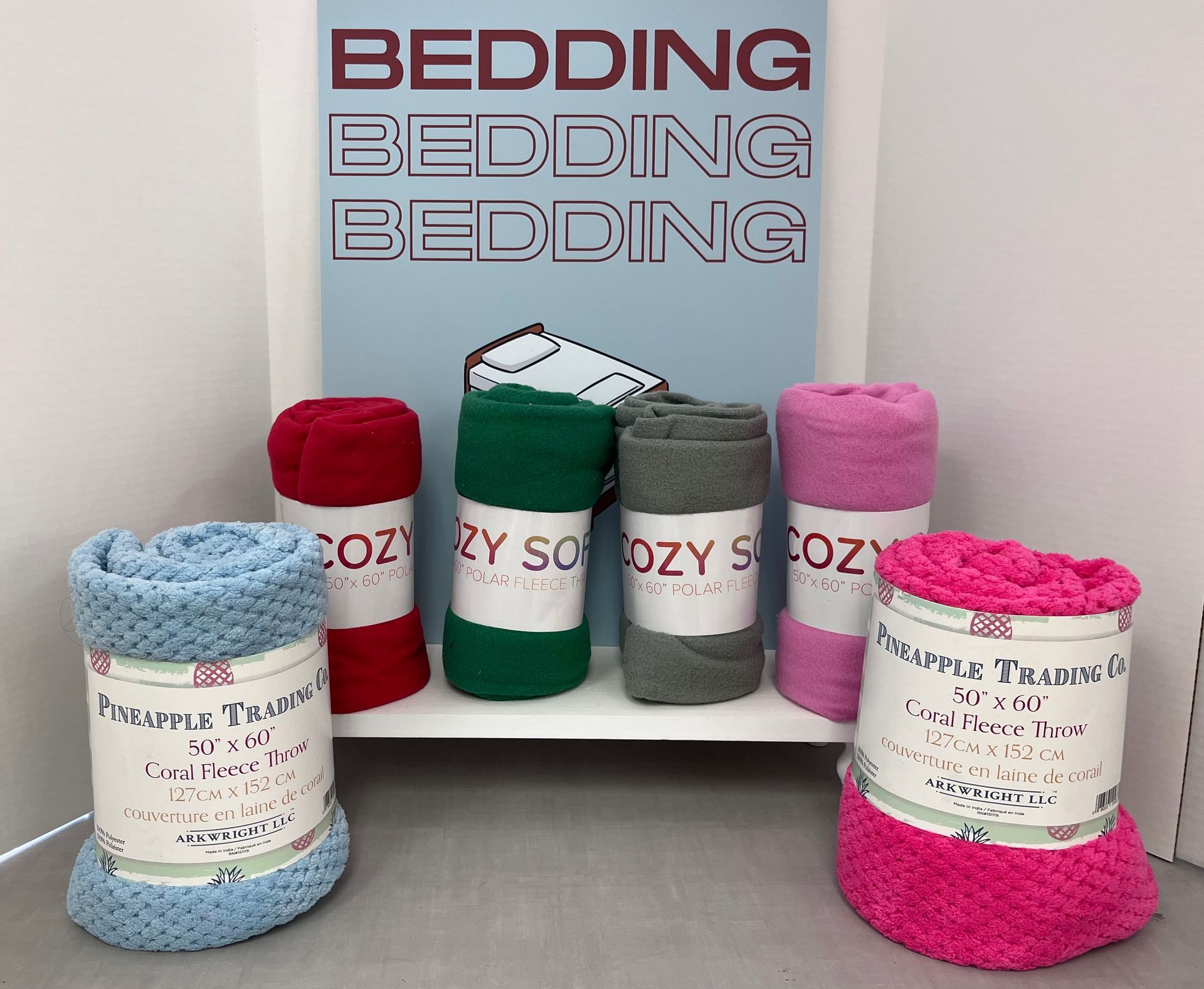 a bunch of blankets are stacked on top of each other in front of a sign that says bedding bedding bedding