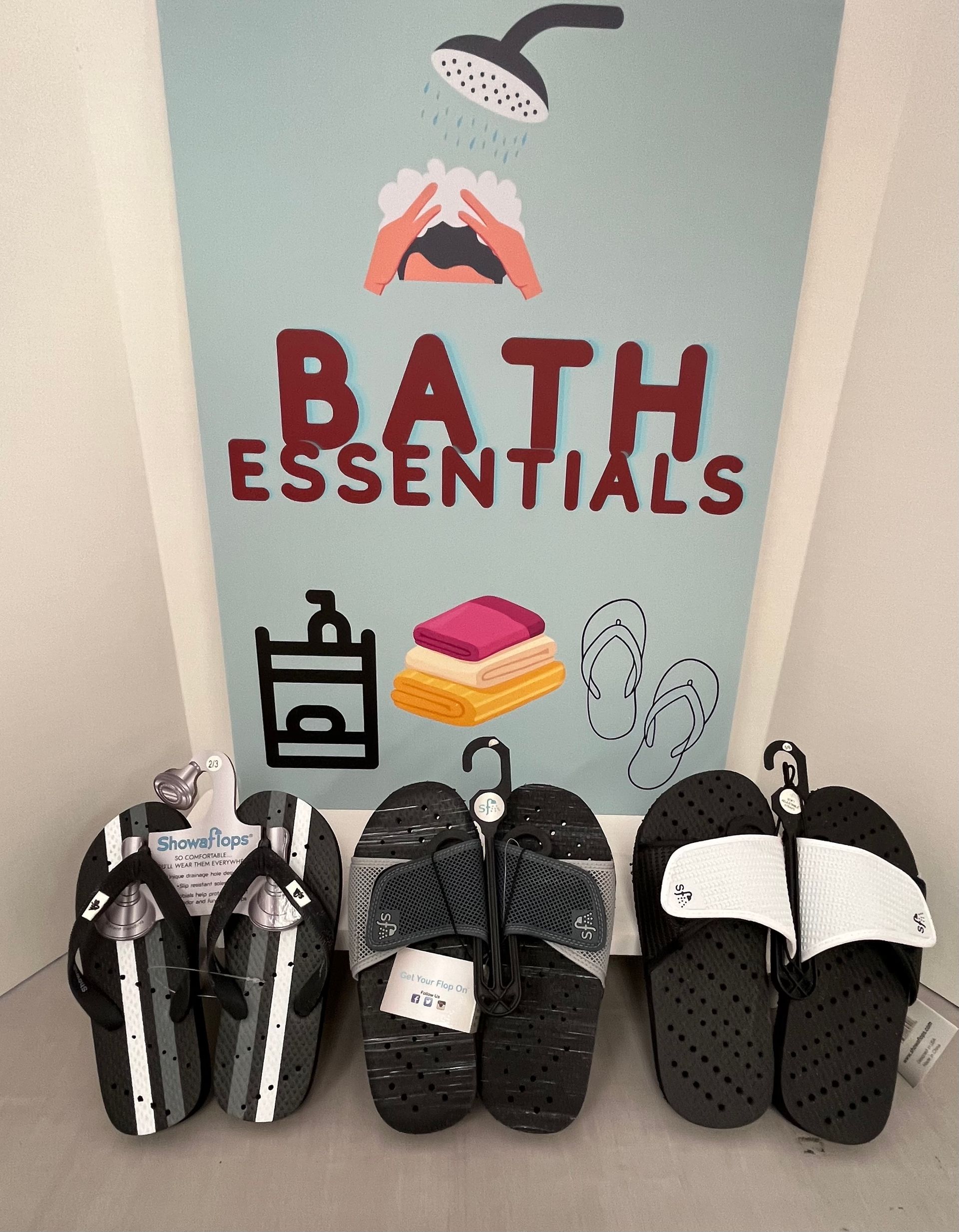 three pairs of slippers are lined up in front of a bath essentials sign