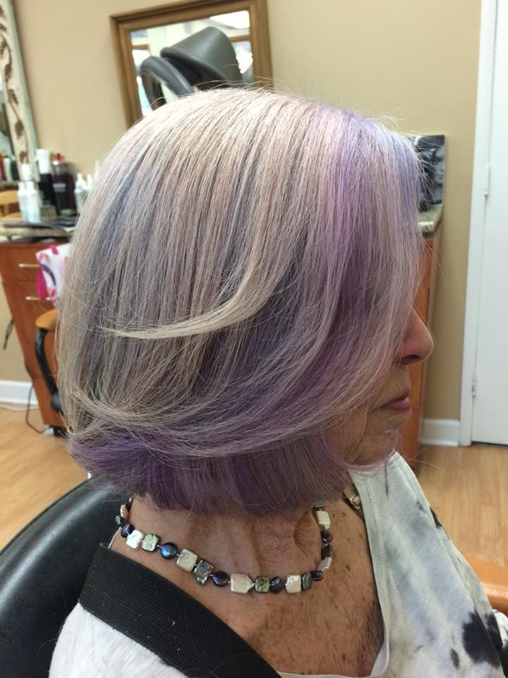 a woman with purple hair is sitting in a chair in a salon .