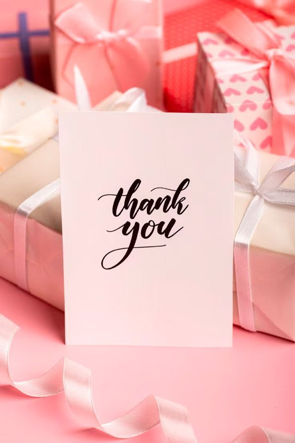 a thank you card is sitting on top of a pile of pink gifts .