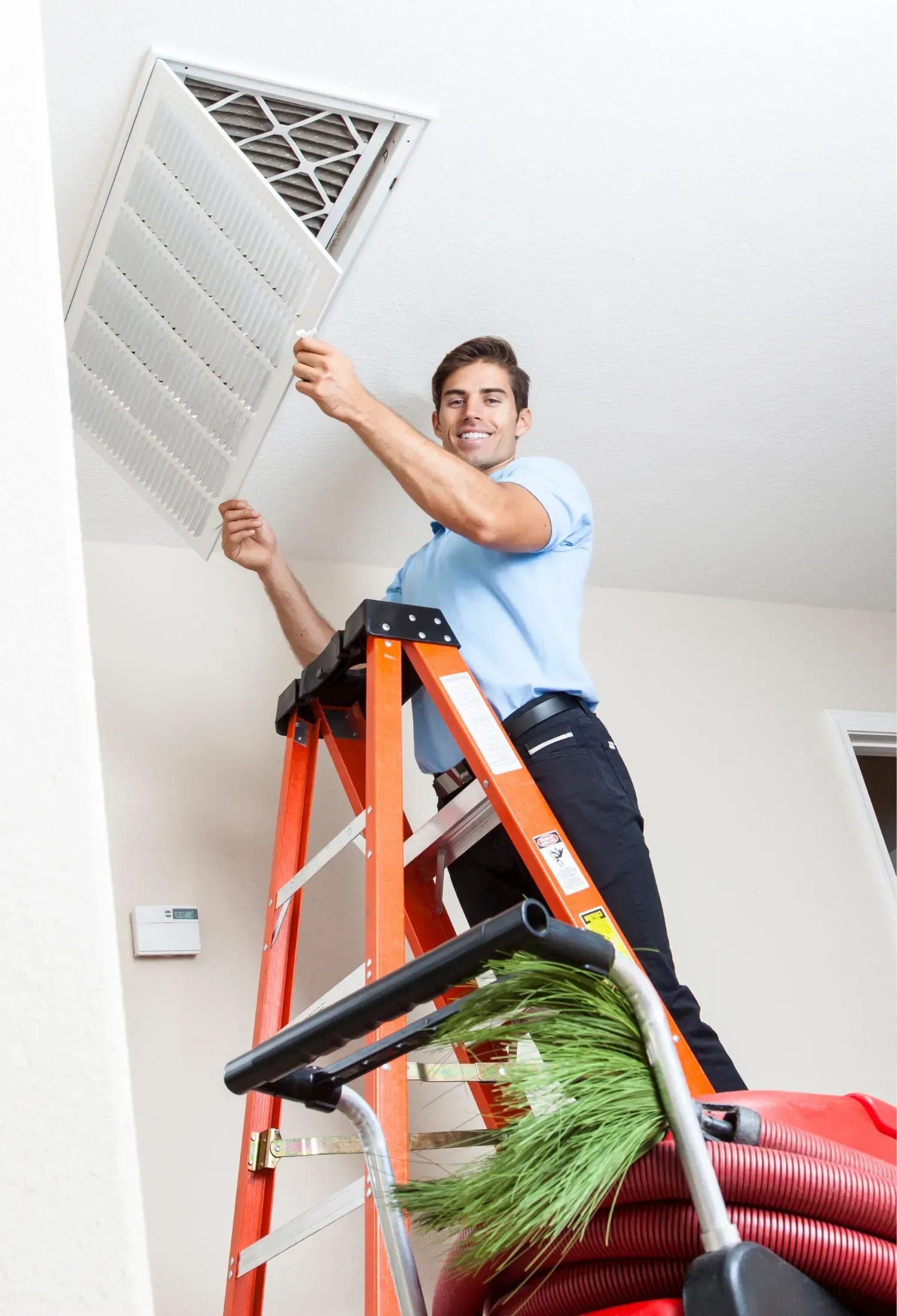 A man is standing on a ladder cleaning an air vent.