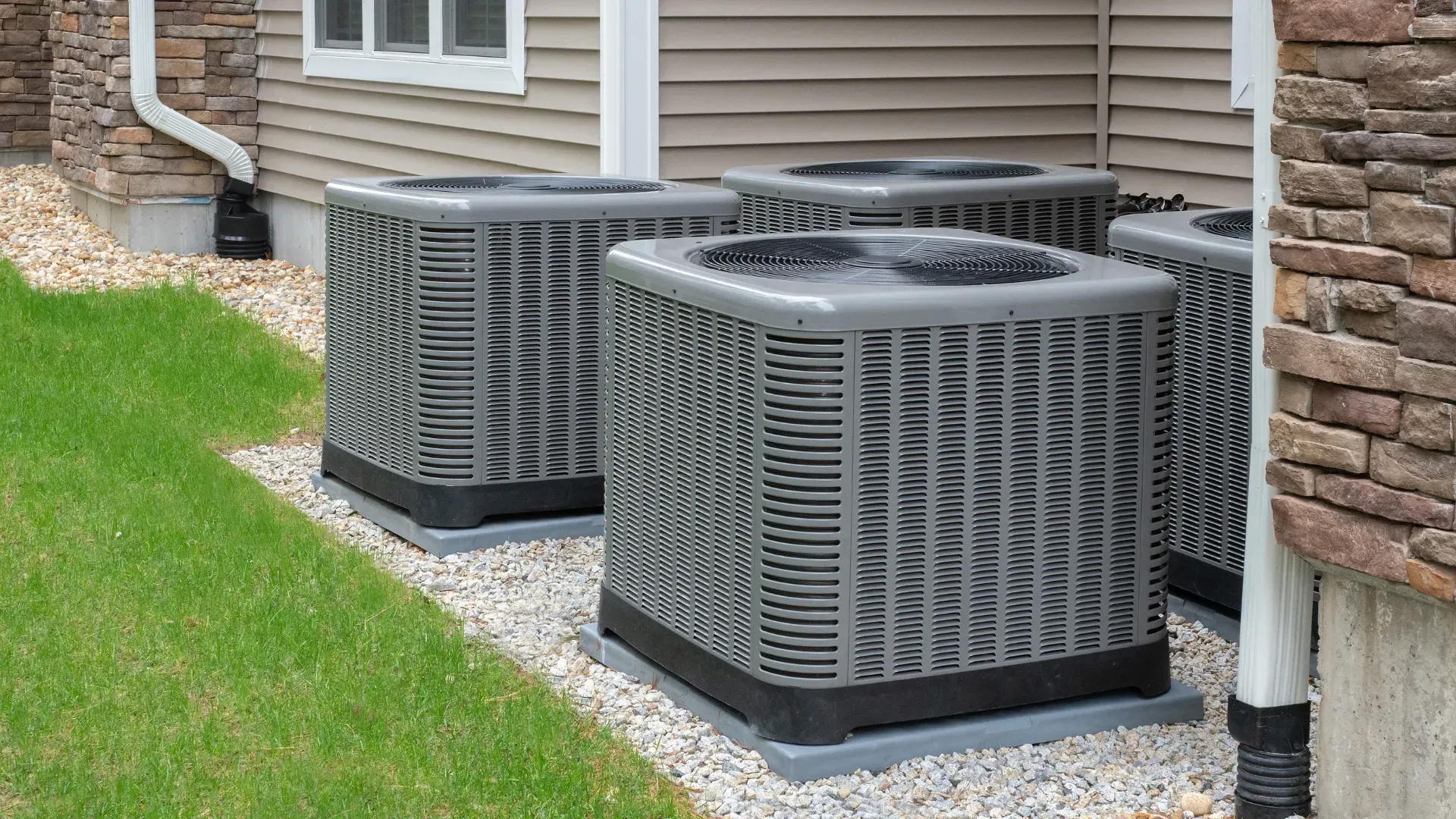 Three air conditioners are sitting outside of a house.